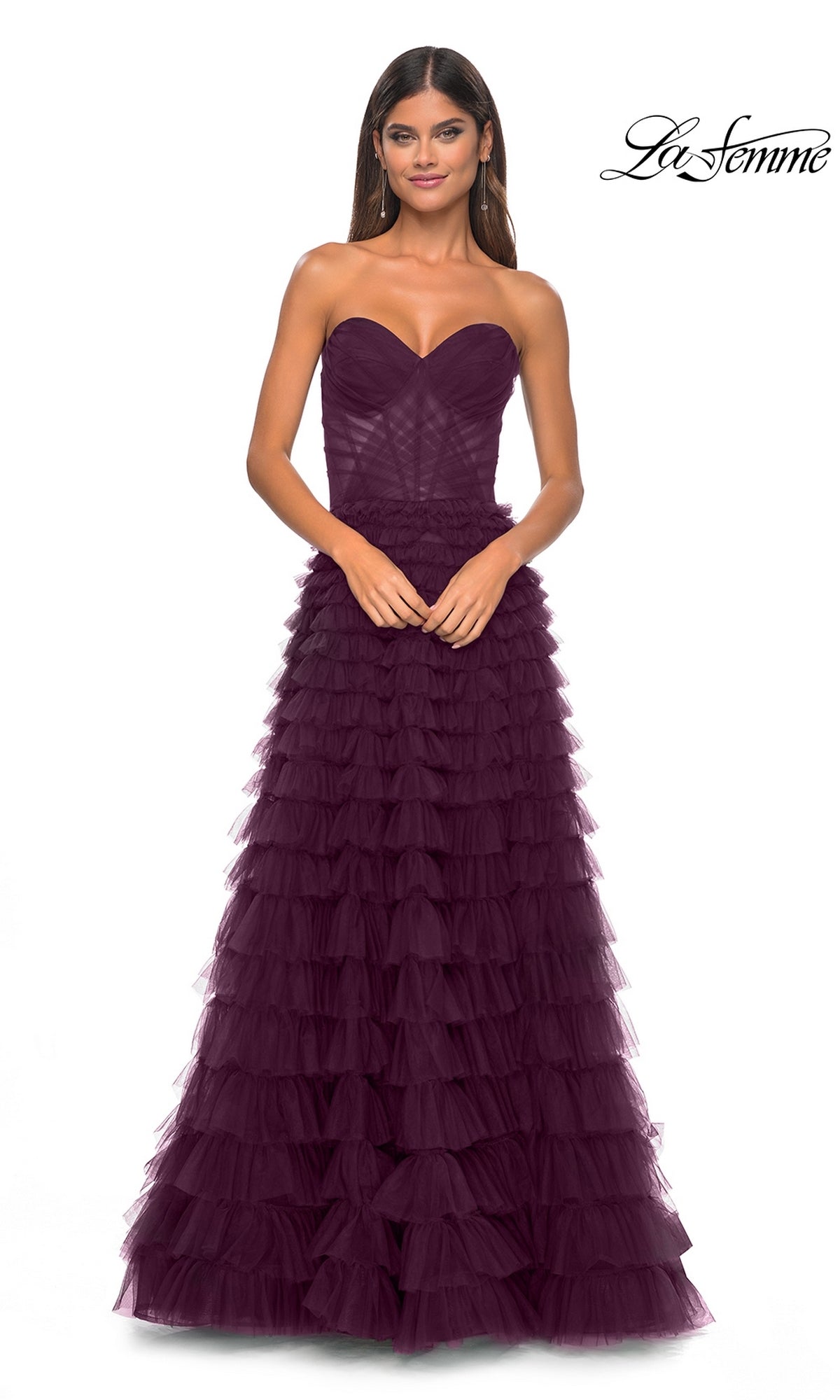 A woman wears the La Femme Strapless Long Ruffled Prom Dress 32283 in dark purple, featuring layered tulle, as she stands against a white background.
